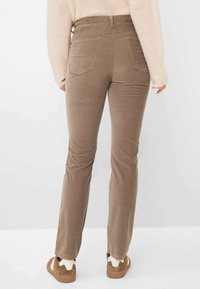 Braune Cord-Hose mit passgenauer Passform, geraden Beinen und zwei Gesäßtaschen. Kombiniert mit hellbraunen Schuhen, die einen lässigen Stil zeigen.