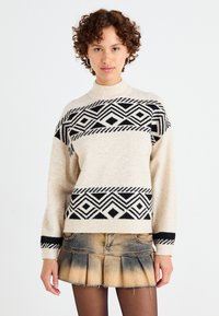 Crème trui met zwart geometrisch patroon en geribbelde halslijn, gecombineerd met een denim minirok met een geplooid ontwerp en vervaagde afwerking.