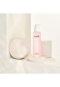 Babor Soothing Rose Toner i en klar flaska, rosa vätska, med ett vitt pumplock, omgiven av texturerade, vita stenrunda objekt.