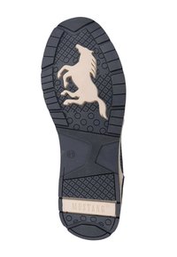 Suela de zapato de goma negra con un diseño elevado de un caballo galopante y la marca "MUSTANG" en un tono beige claro. Texturizada para dar agarre con patrones redondos.