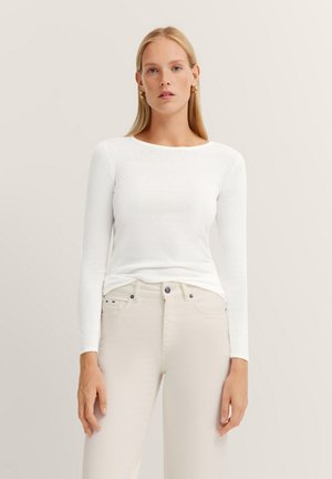 Weißes Langarmoberteil aus leichtem Stoff, kombiniert mit hellbeigen Hosen. Einfaches Design mit Rundhalsausschnitt. Minimalistischer Stil.