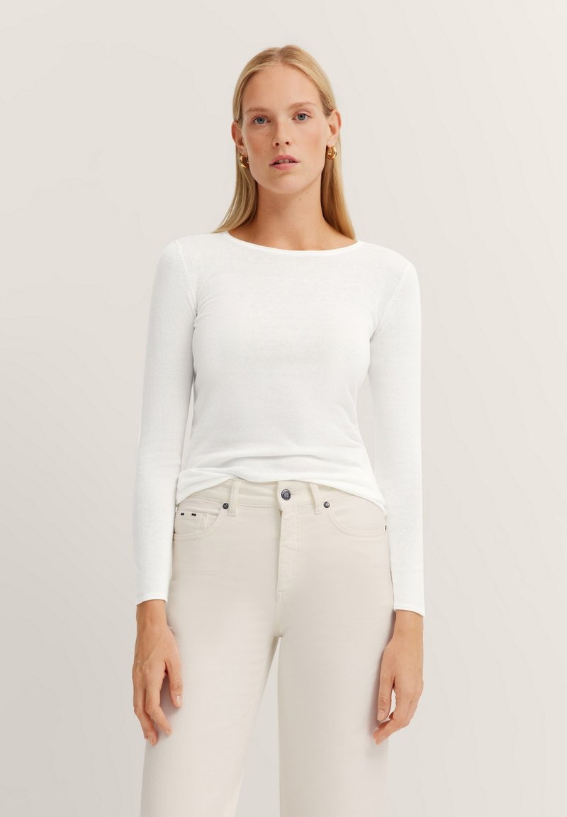 Weißes Langarmoberteil aus leichtem Stoff, kombiniert mit hellbeigen Hosen. Einfaches Design mit Rundhalsausschnitt. Minimalistischer Stil.
