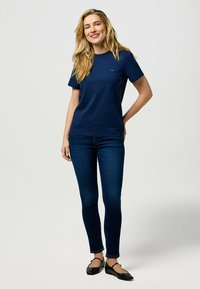 T-shirt en coton bleu marine à manches courtes et encolure ronde, associé à un jean bleu foncé ajusté et des ballerines noires. Design simple, sans motifs.