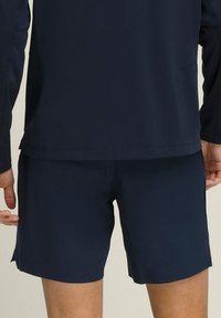 Navyblauwe sportshorts met een gladde textuur, voorzien van een elastische tailleband en zijsplitten voor bewegingsvrijheid.