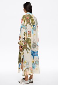 Trükitud pikk kimono, millel on värvilised kujutised lindudest, nägudest ja geomeetrilistest mustritest, kergetes kangastes, külgedel lõhikute jaotusega.