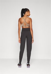 Soutien-gorge de sport marron avec un design de dos découpé, associé à un pantalon noir fuselé et des baskets noires avec des accents roses.
