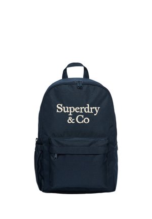Marineblå rygsæk med frontlynlåslomme og "Superdry & Co" broderet i beige foran. Øverste håndtag og justerbare stropper er synlige.