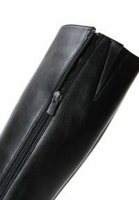 Tige de bottes en cuir noir avec une fermeture éclair fermée et un petit insert élastique en forme de V près du bord supérieur.