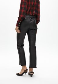 Pantaloni in ecopelle nera con un design aderente e vita media. Abbinati a una camicia a quadri con bottoni dorati e tacchi slingback neri.