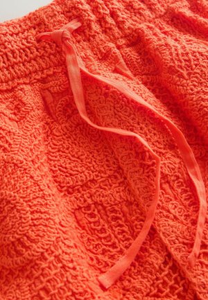 Ryški oranžinė tekstūruota medžiaga su austu raštu ir dviem rišamomis medžiagos juostelėmis, esančiomis viršuje.