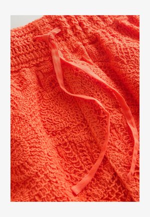 Jasně oranžová texturovaná tkanina s tkaným vzorem a dvěma zavázanými pásky z tkaniny ležícími nahoře.