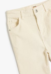 Pantalones de pana beige con un diseño clásico, cinco bolsillos, cintura con pasadores para cinturón y cierre frontal con botón de metal. Tejido texturizado.