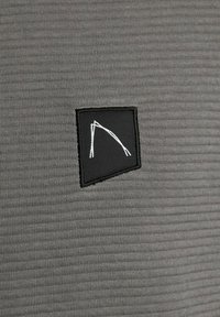 Punto di stoffa nera con un design angolare astratto bianco cucito su un tessuto a coste grigio.