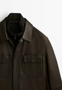 Ruskea nahkatakki, jossa on kaulus, etuvetoketju ja kaksi rintataskua. Sileä pinta klassisella muotoilulla.