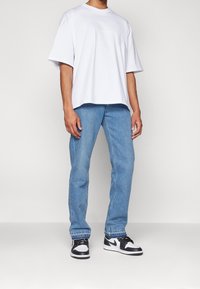 Camiseta blanca de gran tamaño con mangas cortas, combinada con jeans de lavado claro y zapatillas altas en blanco y negro. Un look simple y casual.