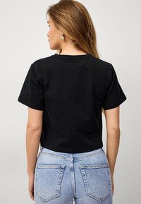 Zwarte cropped t-shirt met korte mouwen, ronde halslijn en een gladde textuur, gecombineerd met lichtblauwe high-waisted jeans.