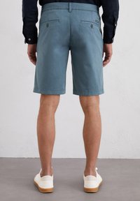 Lichtblauwe shorts van katoen, met een zachte textuur en twee achterzakken met knoopsluitingen. Draag ze met witte sneakers.