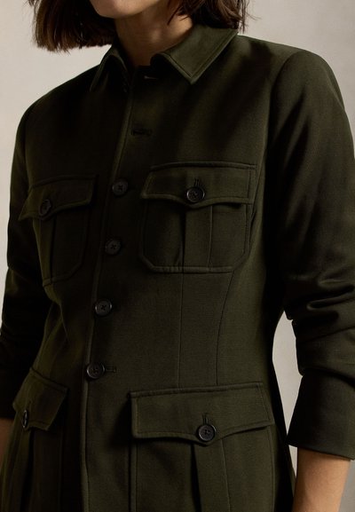 Olijfgroene overhemdjurk met een gestructureerd ontwerp, voorzien van een kraag, knopen aan de voorkant en twee borstzakken met klepsluitingen. Zachte stoftextuur.