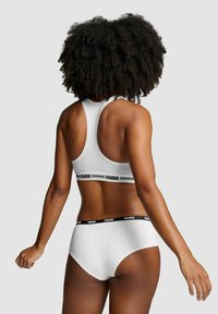 Weiße Sportbra und hochgeschnittene Unterhose mit schwarzem Bund, auf dem das „PUMA“-Logo zu sehen ist. Glatte Textur, Racerback-Design, minimale Nähte.