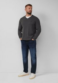 Grijze lange mouwen V-hals trui, slim fit, gecombineerd met donkerblauwe jeans en witte sneakers. Eenvoudig ontwerp met een subtiel logo.