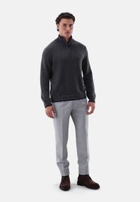 Dunkelgrauer Strickpullover mit Reißverschlusskragen, kombiniert mit hellgrauen maßgeschneiderten Hosen und braunen Schnürstiefeln, präsentiert an einem Model.