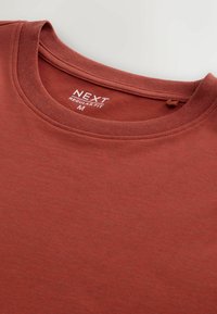 Červené bavlněné tričko s kulatým výstřihem, s hladkou texturou. Na vnitřní straně límce je štítek "NEXT REGULAR FIT M".