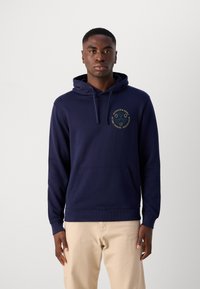 Sweat à capuche bleu marine en coton, doté d'une poche kangourou et d'une capuche avec cordon. Le devant présente un logo circulaire en jaune et vert.