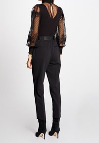 Top nero con maniche a sbuffo in pizzo trasparente e schiena a V, abbinato a pantaloni neri su misura e stivali neri in suede con tacco alto.