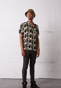 Kortermet skjorte med et svart og kremfarget geometrisk mønster, paret med mørke slim-fit bukser og svarte high-top sneakers. Olivengrønn bøttehatt.