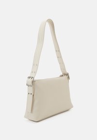 Beige Schultertasche aus weichem Material, mit flacher Form, Reißverschluss und einem strukturierten Tragegurt mit silbernen Nieten und einer Schnallen-Detail.