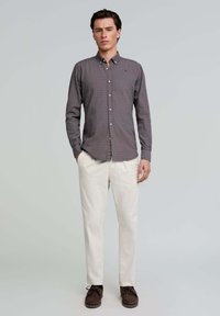 Camisa de hombre de manga larga abotonada en gris oscuro con un patrón de cuadros morados, combinada con pantalones crema y zapatos marrones.