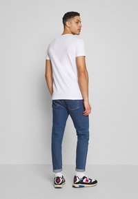 White cotton t-shirt, fitted design, paired with blue denim jeans, rolled cuffs, and black, white, and red sneakers. Simple and casual look.