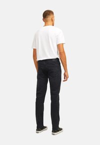 Jeans in denim nero a vestibilità rilassata con un classico design a cinque tasche, abbinati a una maglietta bianca semplice e sneakers nere.