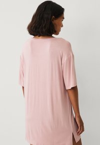 Lyserød oversized t-shirt med korte ærmer, blød stof, rund halsudskæring og sideslids for nem bevægelse. Enkelt design med en glat tekstur.