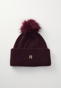 Bonnet en tricot bordeaux avec une texture côtelée, dotée d'un pompon en peluche sur le dessus et d'un petit accent logo doré sur le revers replié.