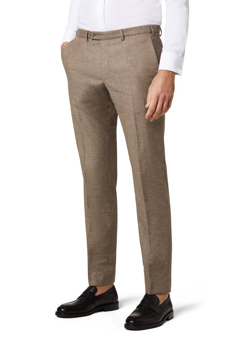Beige maßgeschneiderte Hose aus strukturiertem Material, mit flachem Bund, seitlichen Taschen und slim Fit. Kombiniert mit schwarzen Mokassins.