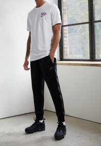 Vit Nike t-shirt med färgglad logga, kombinerad med svarta sweatpants med sidologga, och svarta sneakers med en texturerad sula.