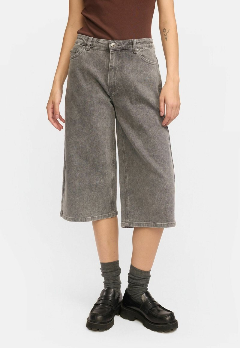 Culottes en denim gris avec une jambe large, taille mi-haute et design traditionnel à cinq poches. Associés à des chaussures à plateforme noires et des chaussettes grises.