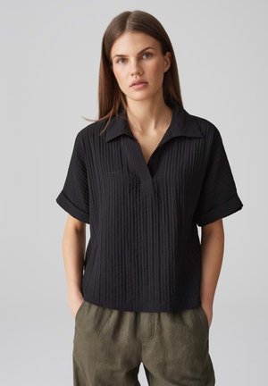 Schwarzes, kurzärmeliges Shirt aus strukturiertem, geripptem Stoff mit Kragen, teilweise Knopfleiste und lässiger Passform.