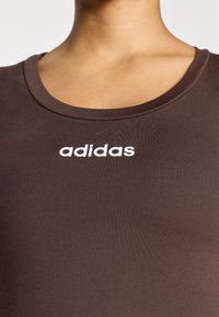 Brown athletic top made of smooth fabric with a round neckline. Features "adidas" logo in white across the chest. Simple design, no patterns.