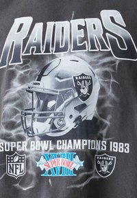 Črna majica s kratkimi rokavi z grafikami čelade Raiders, besedilom "RAIDERS" in "SUPER BOWL CHAMPIONS 1983" v belem. Vključeni so logotipi NFL.