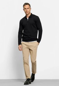 Schwarzes Langarm-Poloshirt mit Reißverschluss am Kragen, kombiniert mit beigen Chinos und schwarzen Lederschuhen. Glatter Stoff, maßgeschneiderte Passform, minimalistisches Design.