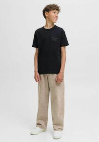 Črna bombažna majica s majhnim belim potiskom "ORIGINALS Studio". V kombinaciji z svetlobezž žepi širokimi hlačami in belimi supergami.