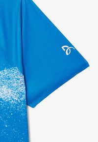 Lyhythihainen urheilupaita elävässä sinisessä, jossa on liukuvärjäyskuvio alareunassa ja pieni valkoinen logo hihassa.