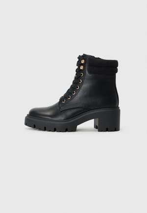 Bottine en cuir noir avec un col en tricot texturé, des accessoires en or et une semelle en caoutchouc épaisse dotée d'un motif de semelle.