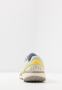 Scarpa da trail running in grigio chiaro e giallo-verde, con una tomaia testurizzata, un tallone imbottito e una suola in gomma con lugs di trazione triangolari.