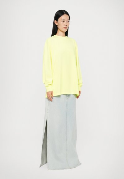 Neon yellow long-sleeve top paired with a light blue denim maxi skirt featuring a side split and visible stitching details.