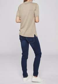 Beige kortärmad tröja med ribbad textur, rund halsringning och sidospjälor, kombinerad med mörkblå slim fit-jeans och vita sneakers.