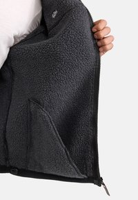 Chaqueta de forro polar gris con cierre de cremallera, que presenta un interior y exterior suaves y texturizados, además de bolsillos laterales.