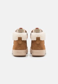 Tan suede high-top shoes with white faux fur collar, rear pull tab, and beige rubber sole. Features branded detail on the sole.